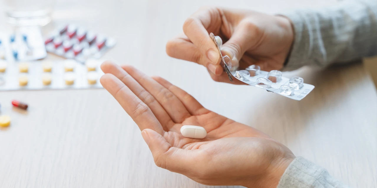 A person removes medicine from a blister pack before taking a tablet, showing prescription drug use connected to medicine addiction.
