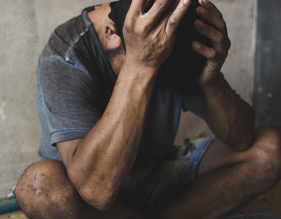 Man sitting on a concrete floor holding his head in both hands, illustrating ketamine withdrawal.