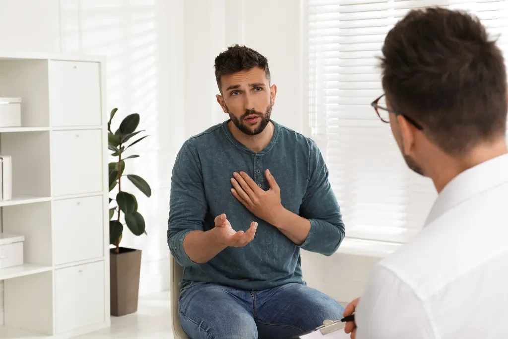two-man-in-conversation Two men in conversation in a therapy room, one acting as the doctor and the other as the client, who appears concerned.