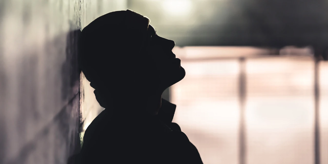 A person leans against a wall in the dark, reflecting the loneliness, emotional struggle and hopelessness often linked to drugs addiction.