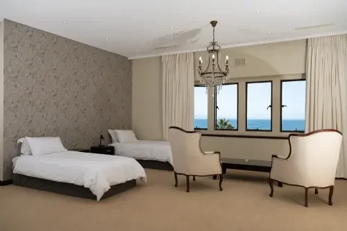zuid-afrika-slaapkamer Slaapkamer met daarin twee enkele bedden en twee fauteuils in crèmekleur en een kroonluchter.