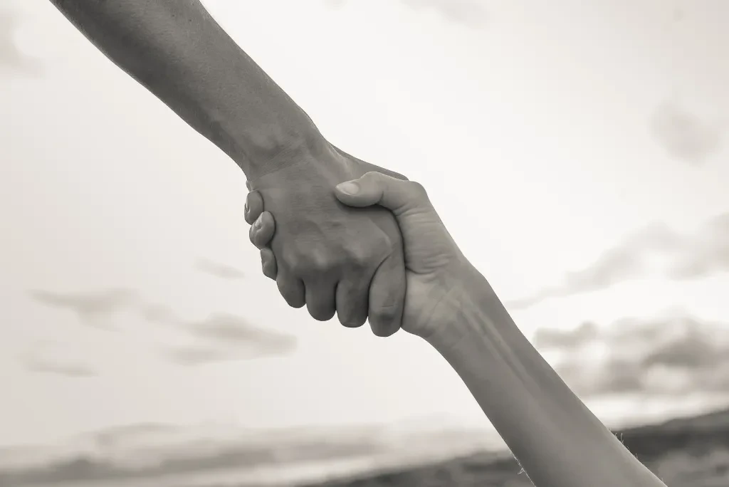 Two hands holding each other with the sky in the background, in black and grey colors.