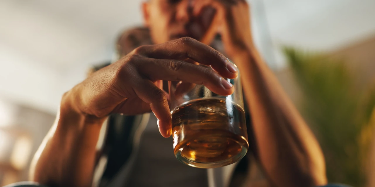 A close-up image of someone holding a glass of alcohol while sitting alone, reflecting the isolation and emotional burden linked to alcohol addiction.
