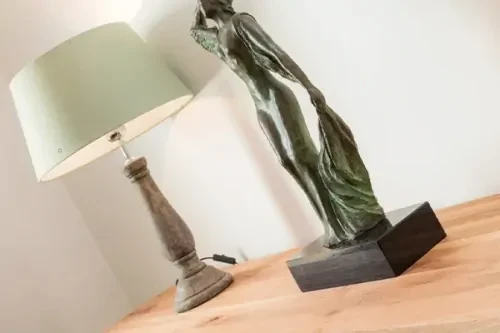 Groen gekleurd beeld van een vrouw op een houten ondergrond en een lamp met mintgroene lampenkap, tegen een witte muur.