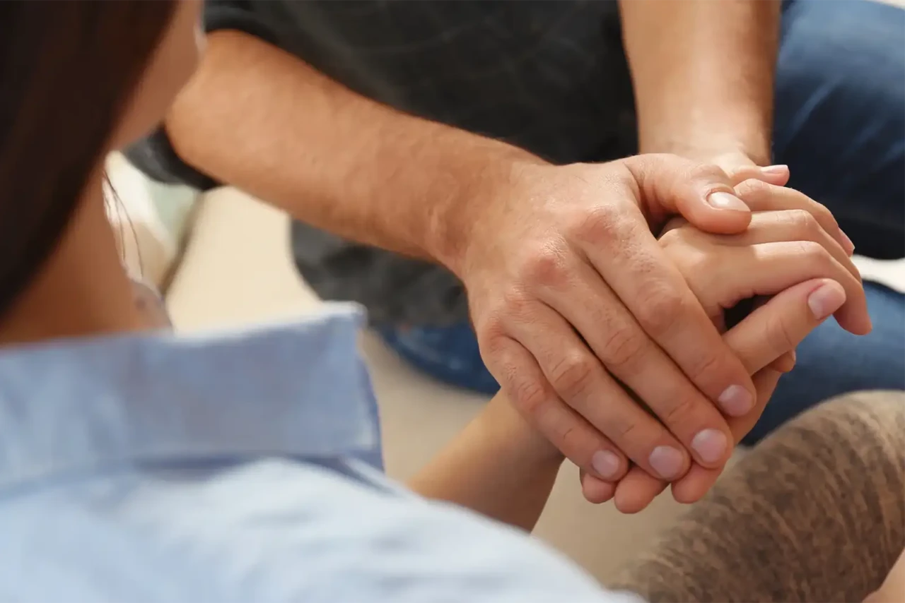 A close-up of hands holding each other in a comforting manner.