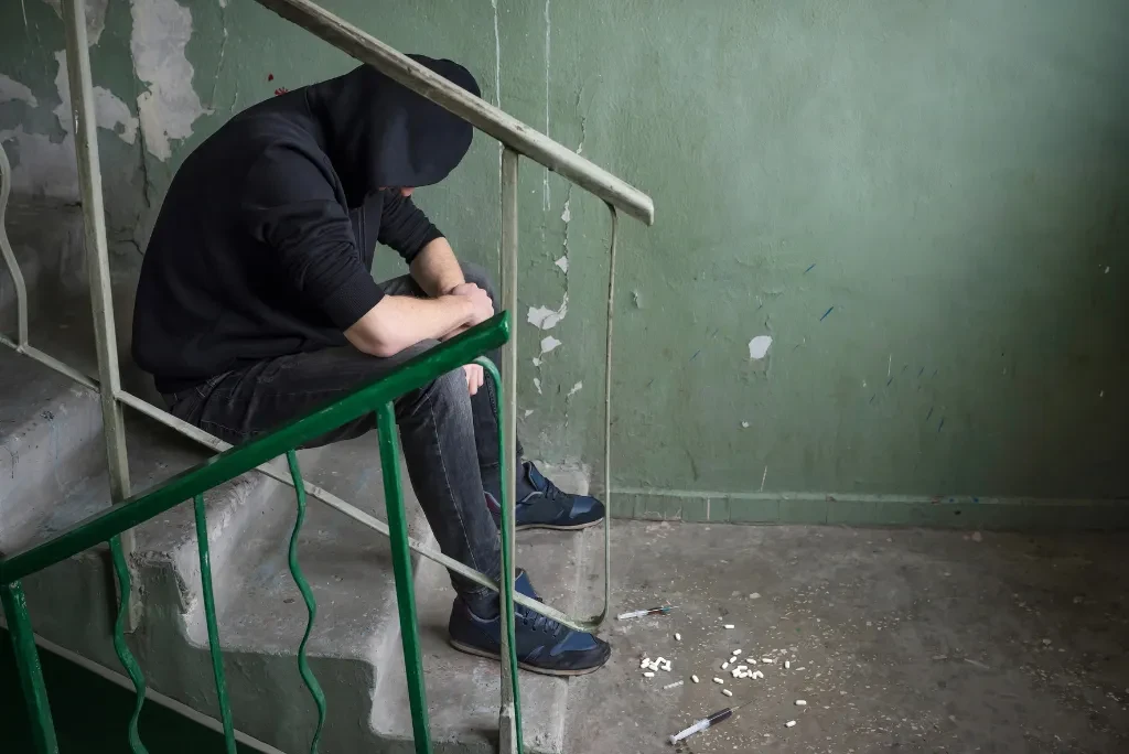 man-on-stairs A man in a black hoodie and jeans sitting on a staircase, with his arms resting on his knees and his head bent.