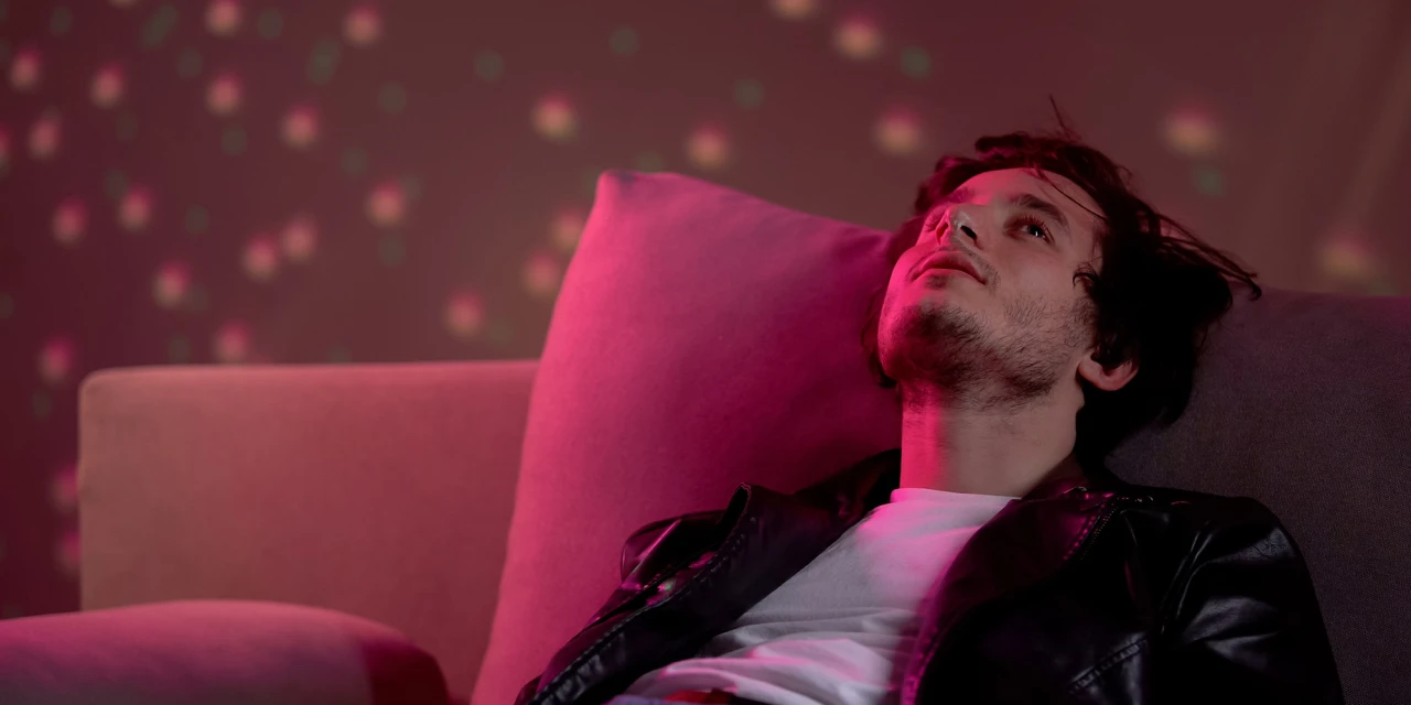 Man lying back on a sofa under pink party lights, staring upward, illustrating ecstasy effects.