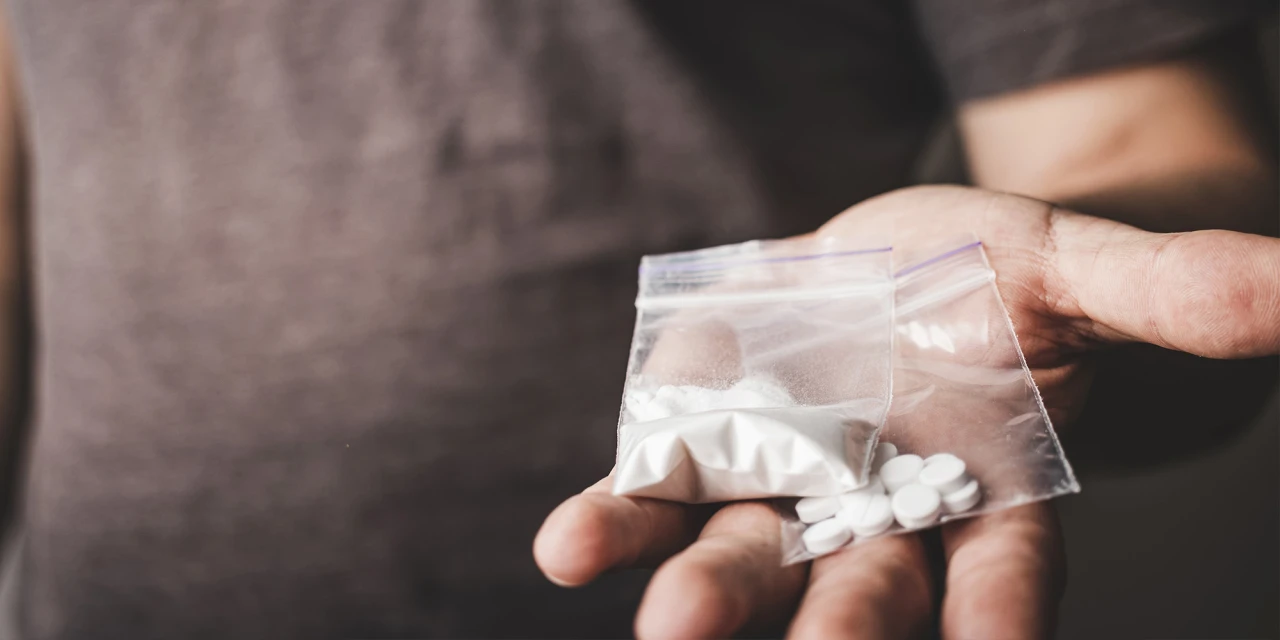 A person holds a small bag containing white powder and pills, representing substance misuse and the risks connected to LSD addiction.