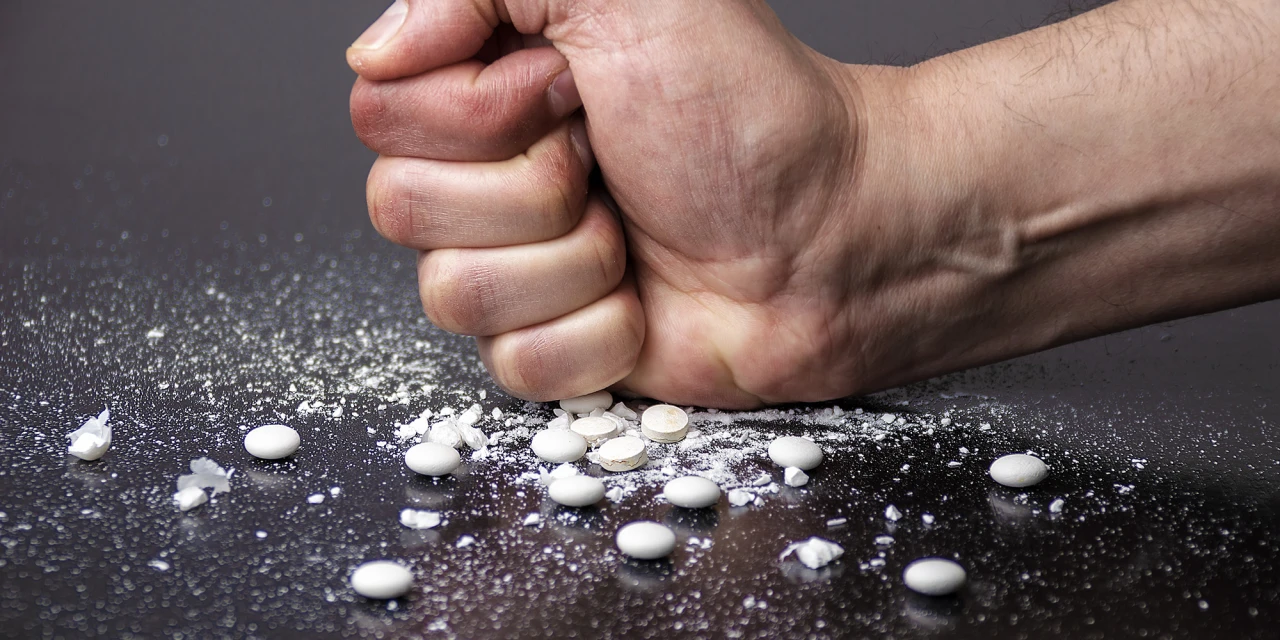 A clenched hand crushes pills on a dark surface, symbolising frustration, compulsive drug use and the destructive impact of speed addiction.