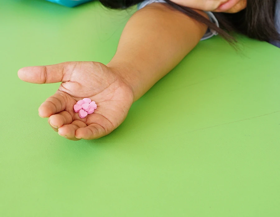 Pink heart-shaped ecstasy pills in an open hand, person slumped over a green table.