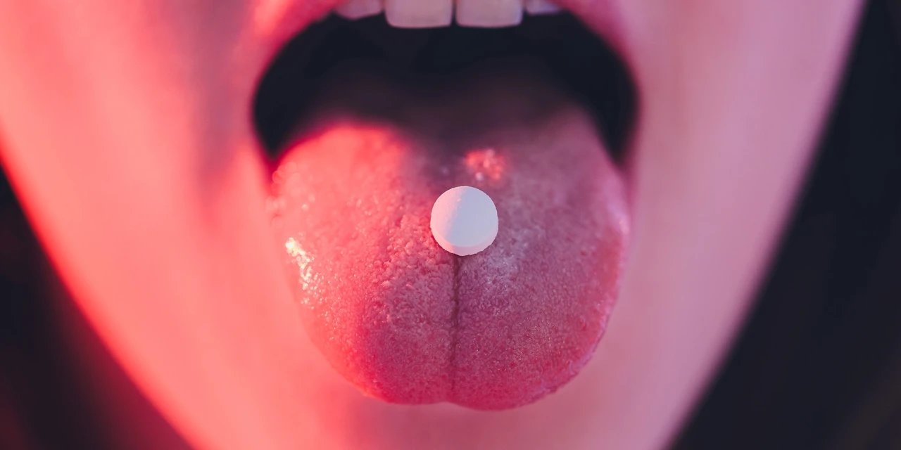 A close-up image of an ecstasy pill placed on a person’s tongue, illustrating recreational drug use linked to ecstasy addiction.