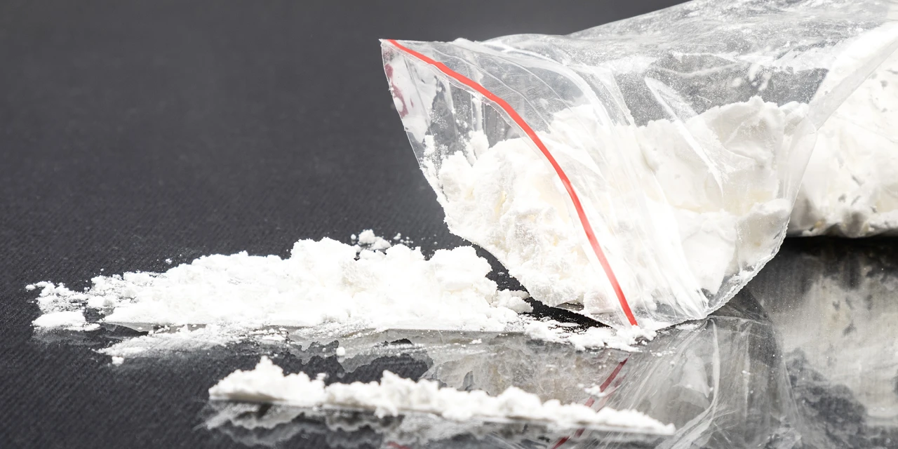 A plastic bag filled with white powder sits on a reflective surface, representing illegal substances connected to amphetamine addiction and long-term health risks.