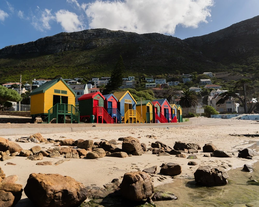 Colourful beach huts on the beach with mountains in the background.