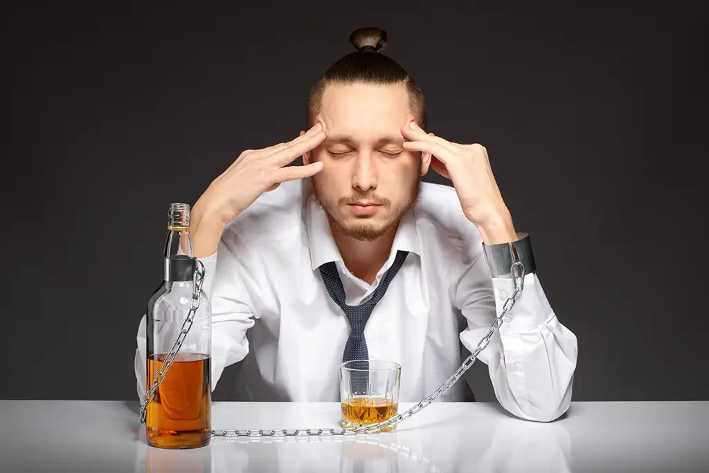 man-chained-to-alcohol A man holding his head in his hands, looking concerned and chained to a bottle of liquor.