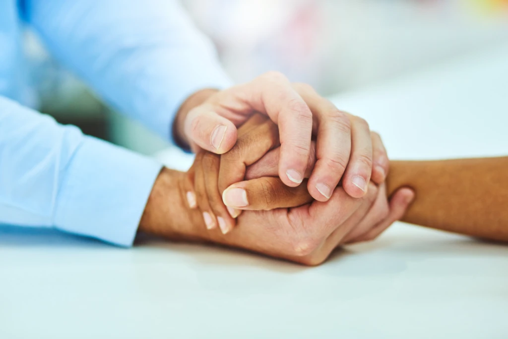 holding-hands-blurry-background Two people holding hands in a comforting way, with a blurry, light background.