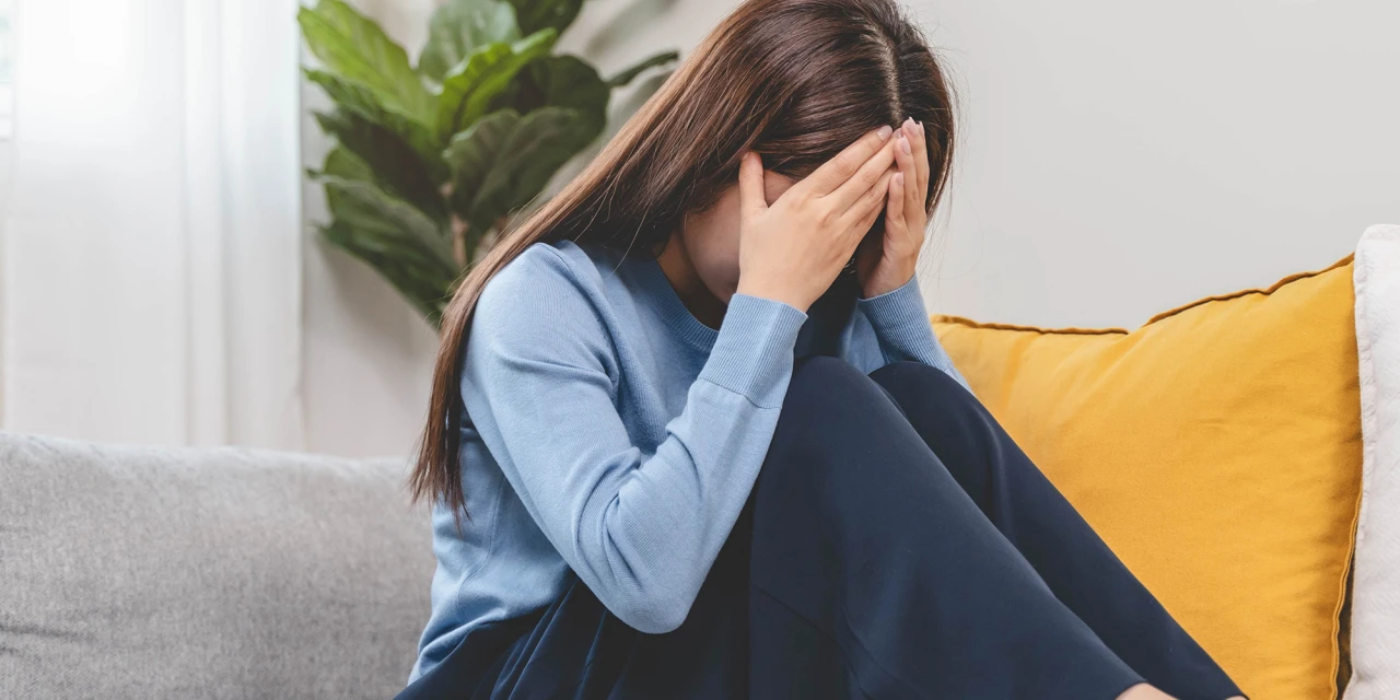 A woman sits on a sofa with her head in her hands, showing the emotional stress and overwhelm that can come with behavioural addiction.