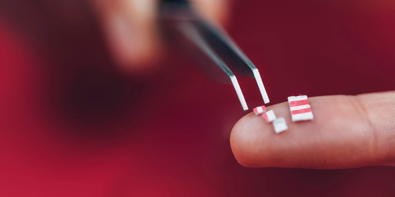 Small LSD tabs are held on a fingertip with tweezers, illustrating the use of hallucinogenic substances linked to LSD addiction.