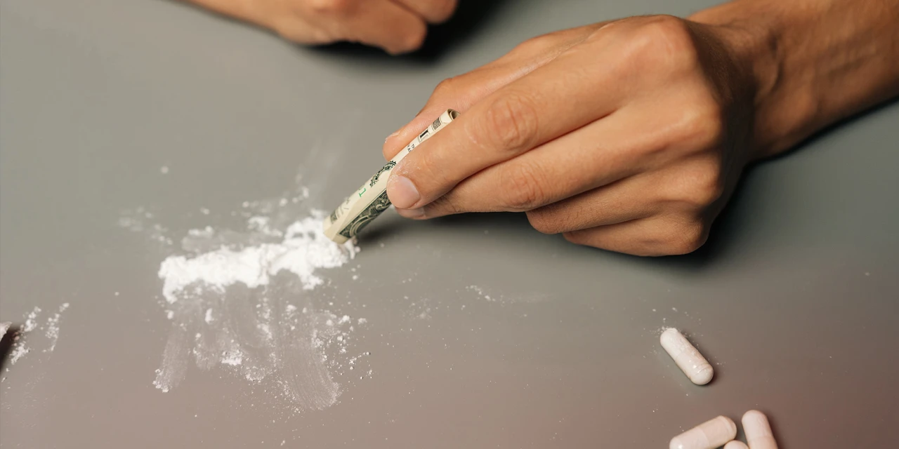 Hand using a rolled banknote to snort cocaine, illustrating drug addiction and recovery.