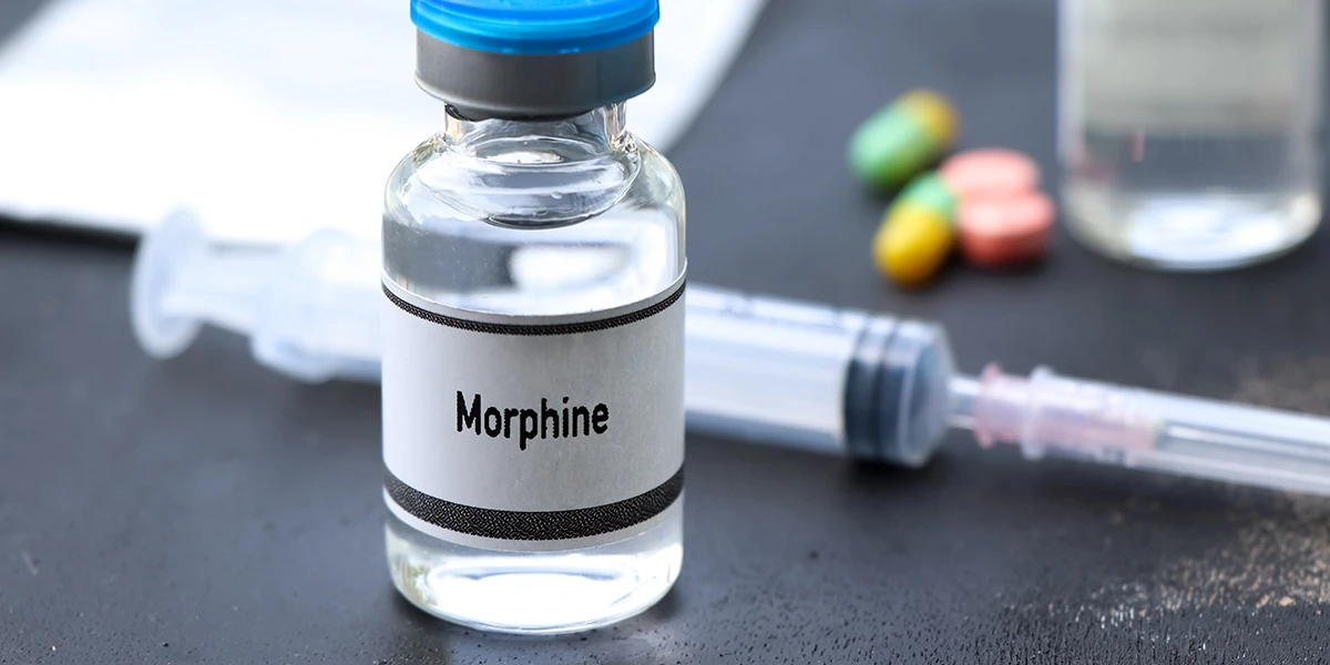 Vial labelled morphine next to a syringe and capsules, illustrating morphine addiction.