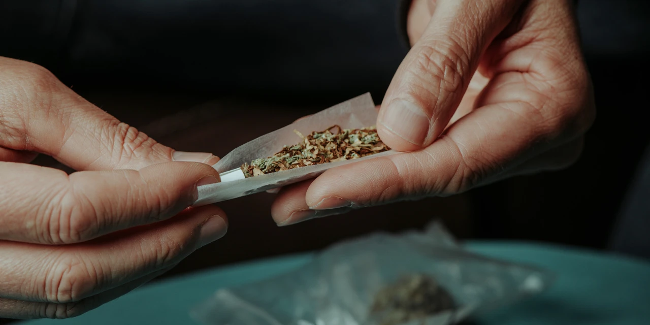 Hands roll a marijuana joint using rolling paper and cannabis, showing drug preparation commonly associated with marijuana addiction.
