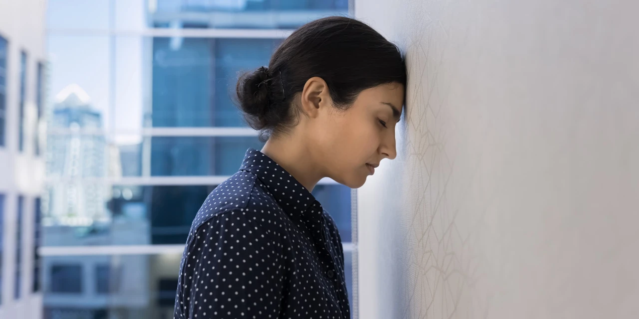 A woman leans against a wall in silence, reflecting feelings of burn out, mental exhaustion and emotional stress in daily life.