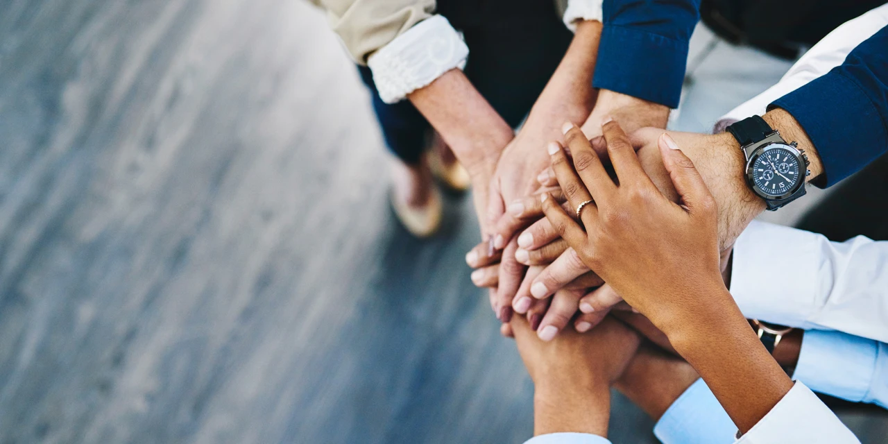 A diverse group of people standing together, stacking their hands in the center of the circle.
