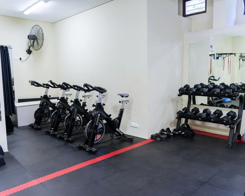 Fitness room with exercise bikes, dumbbells and a mirrored wall.