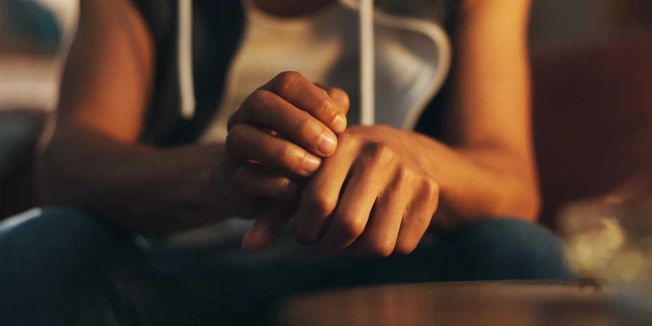 Person in a hoodie sitting with tense, clasped hands, illustrating ketamine rehab.