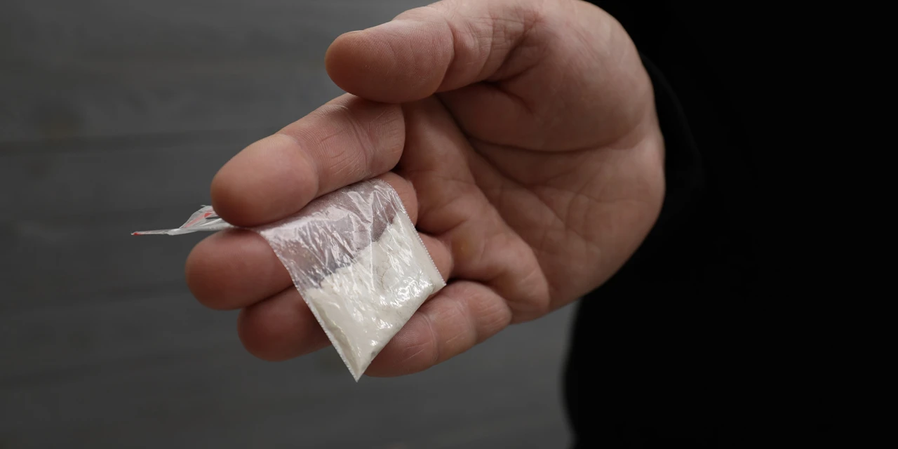 A person holds a small plastic bag filled with white powder, symbolising illegal drug use and the destructive effects of cocaine addiction.