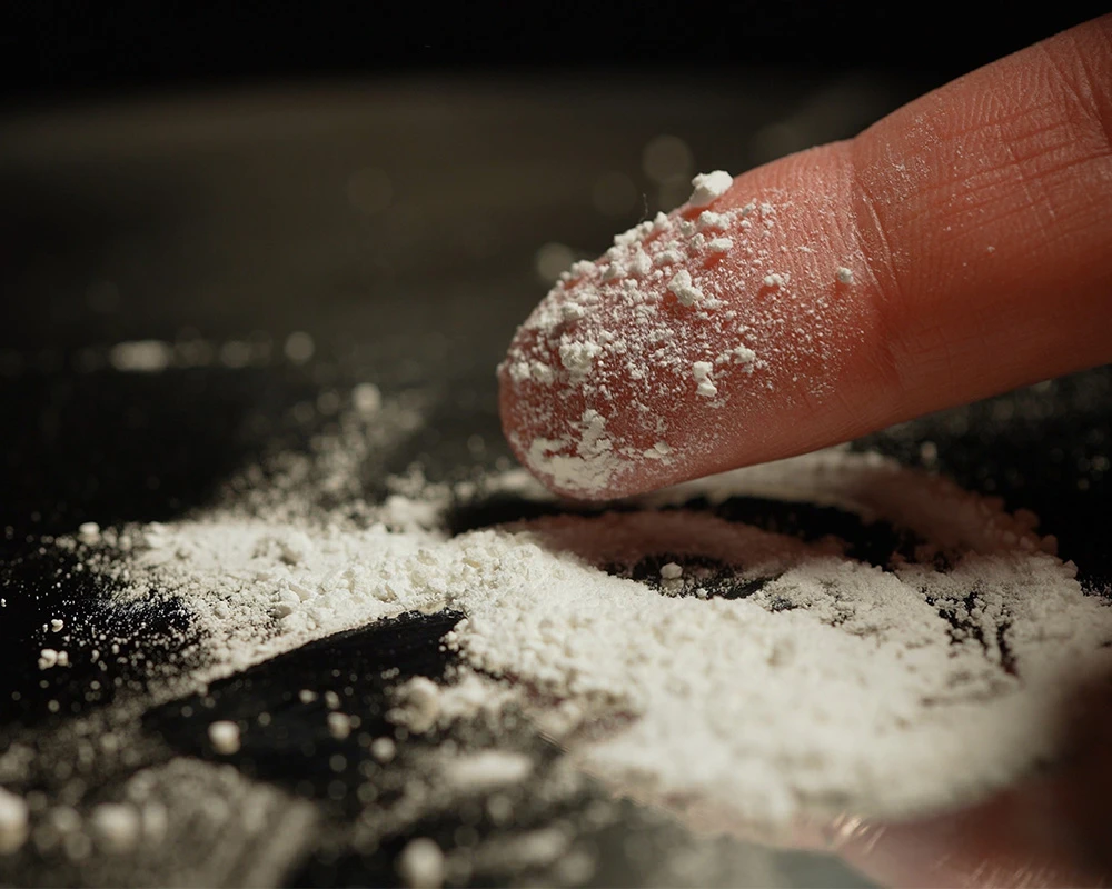 A finger swipes designer drugs onto the table.