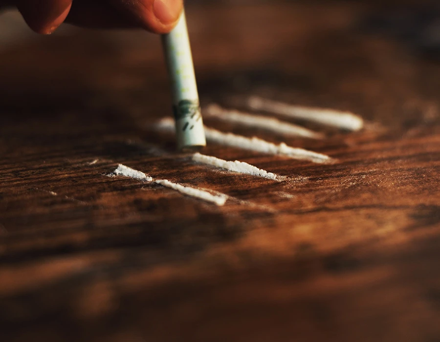 Rolled-up banknote over lines of white ketamine powder on a wooden table.