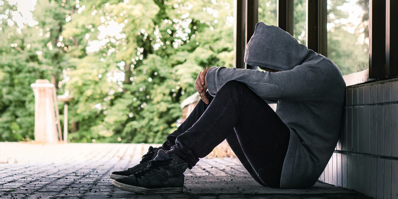 A person sits alone with their head down outside, illustrating the isolation, emotional impact and loneliness that can come with addiction.
