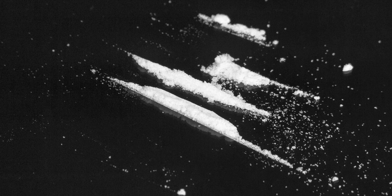 Several lines of cocaine lie on a dark surface with powder scattered around them, representing substance misuse and the risks linked to cocaine addiction.