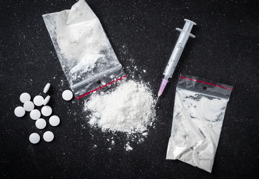 Powder, pills and syringe on dark surface symbolizing drug addiction