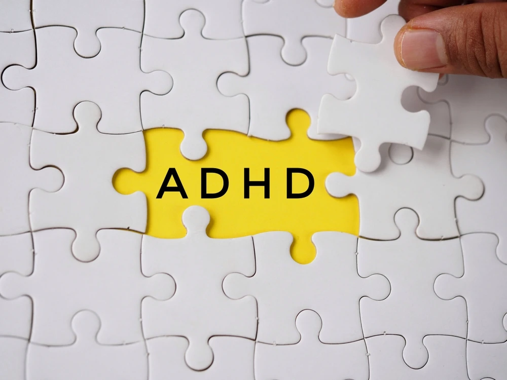 White puzzle pieces surround a yellow piece labeled “ADHD,” symbolizing addiction.