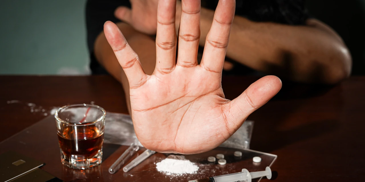 Hand raised in refusal beside cocaine, pills, and alcohol, representing cocaine withdrawal symptoms.