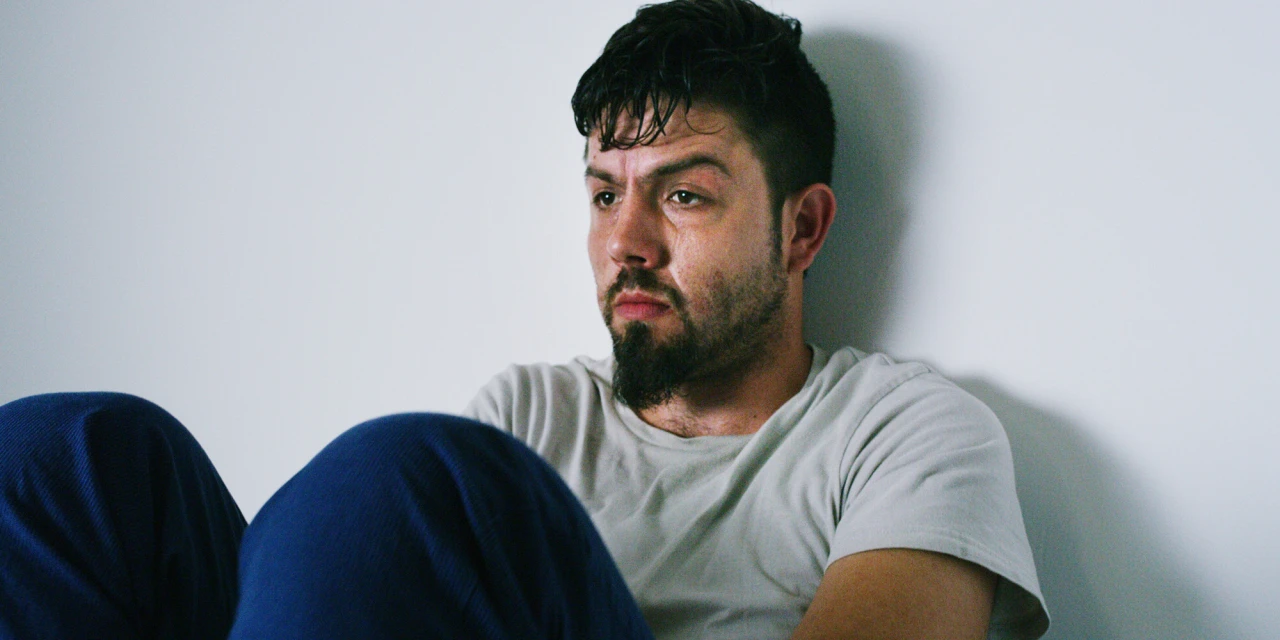 Sweaty man sitting on the floor against a white wall, illustrating ketamine withdrawal symptoms.